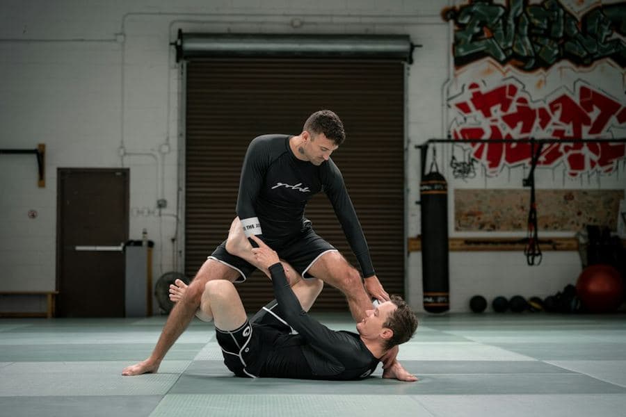 Two athletes grappling on the mats of a raw gym, graffiti on the wall behind them