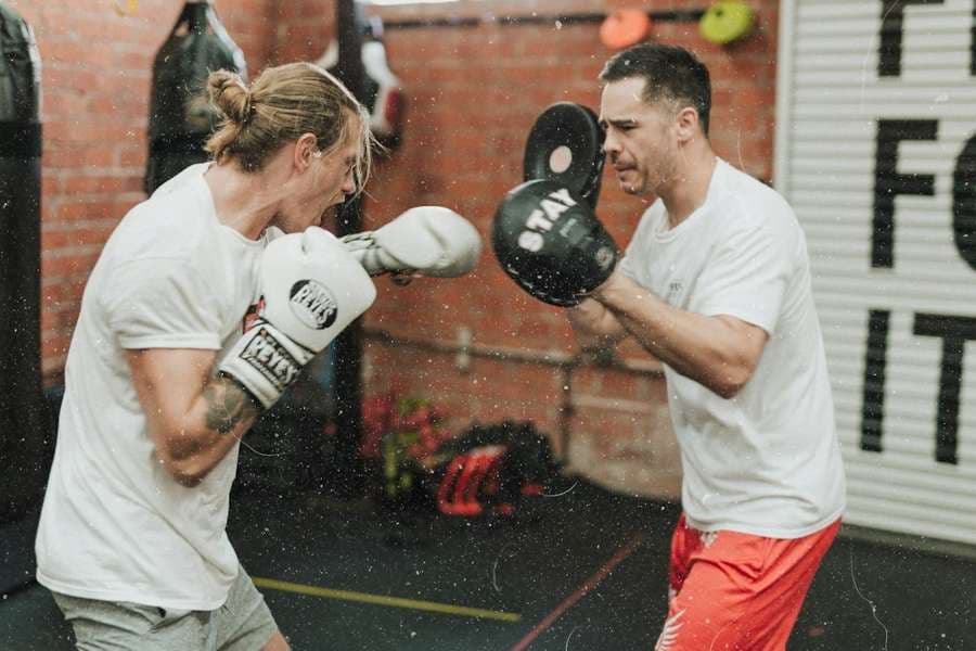 A coach holding pads while an athlete throws a punch in a brick-walled gym